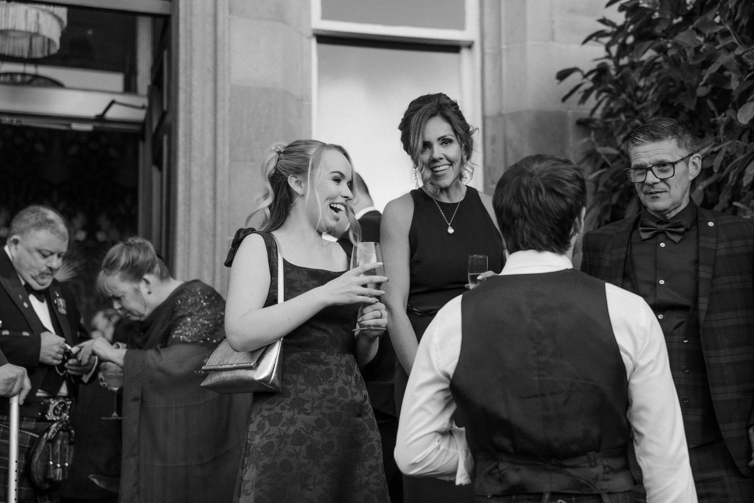 Wedding guests laughing and socializing during a black and white reception celebration.