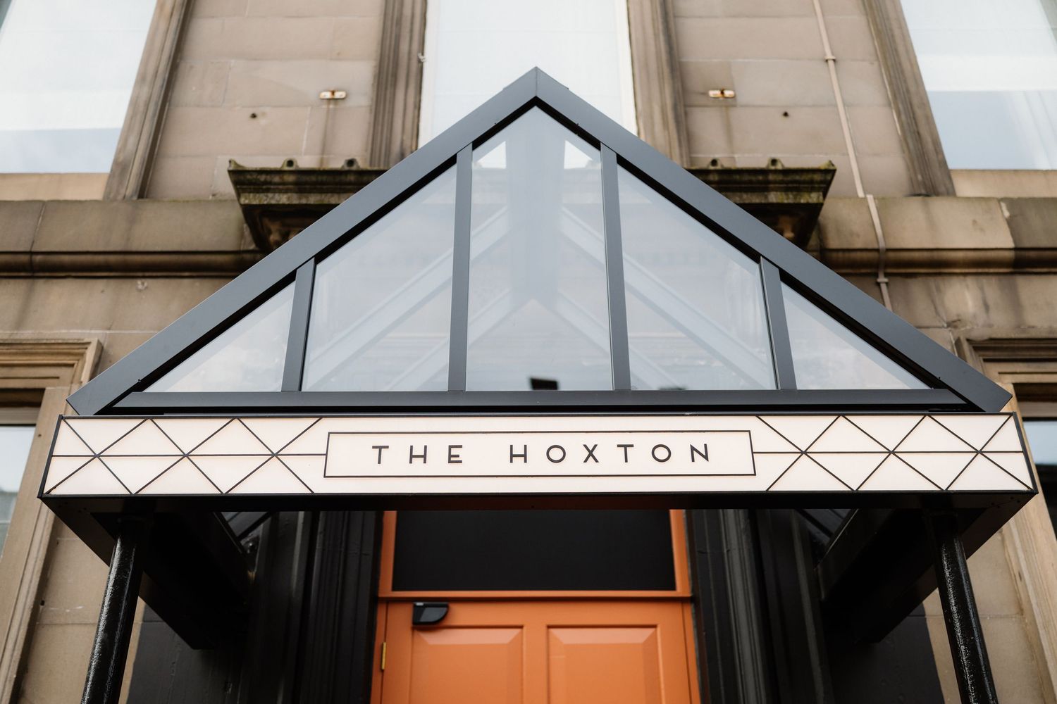 The Hoxton hotel entrance with geometric glass canopy, Art Deco signage, and orange door.