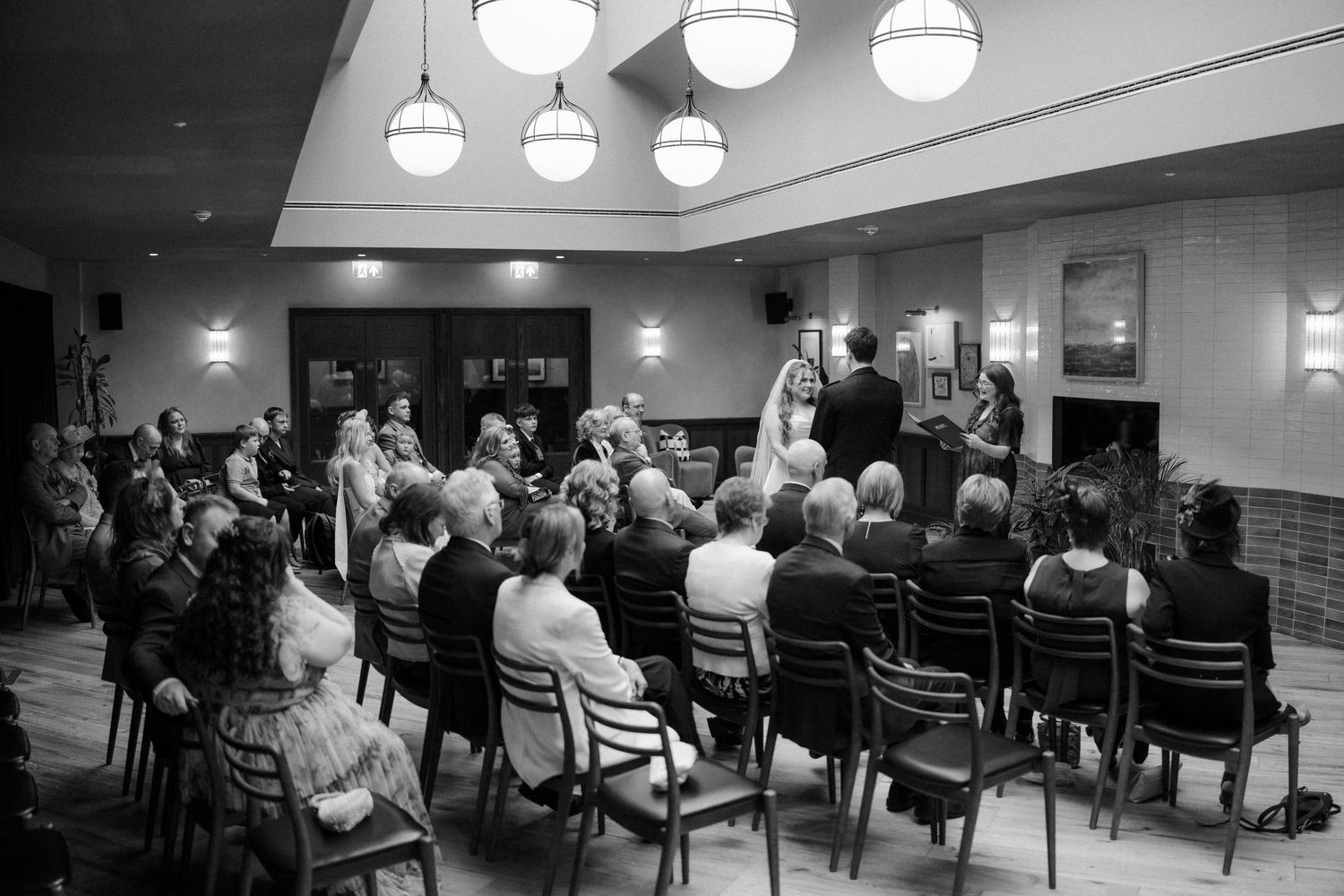 Black and white photo of wedding ceremony guests seated in rows facing the couple at the altar.