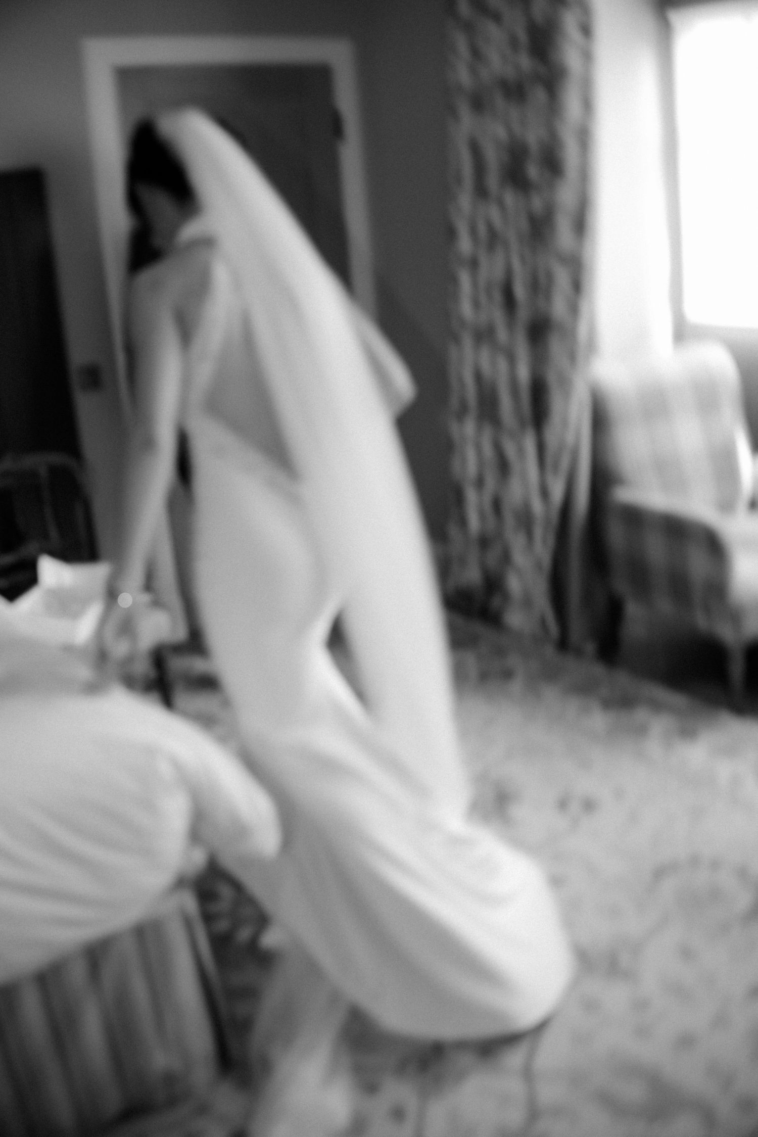 Black and white blurred artistic photo of a bride in a white wedding gown and veil in a hotel room.