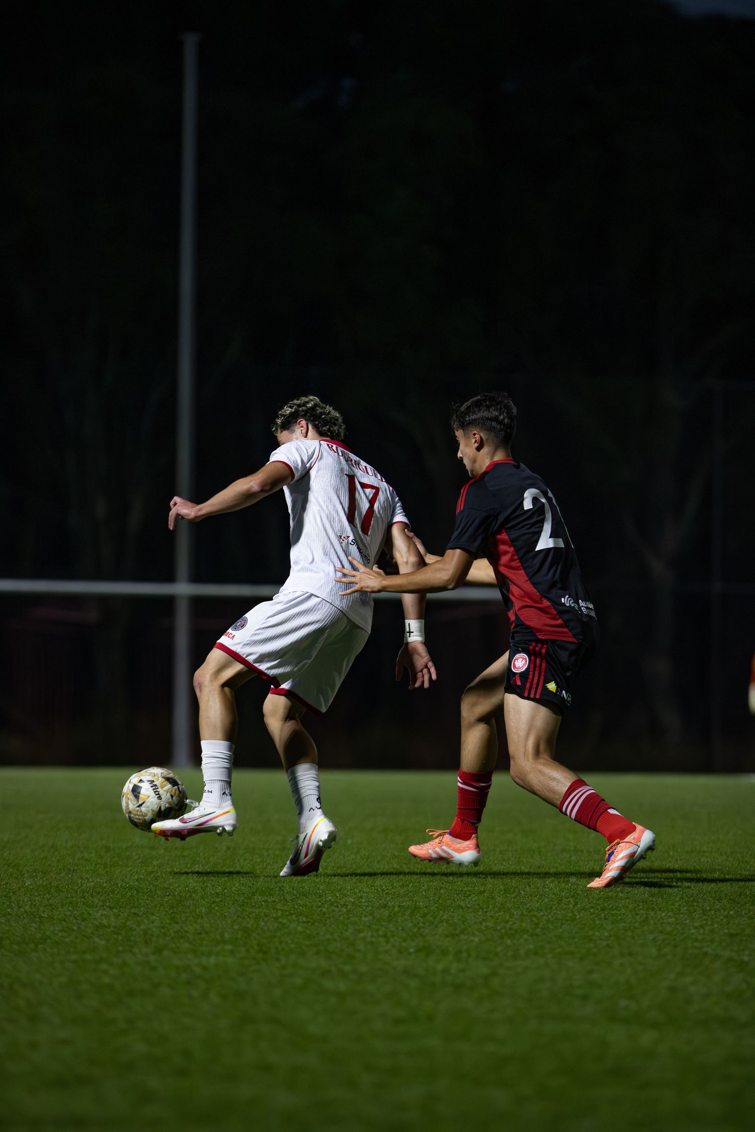 Two soccer players compete for ball during night match on green field.