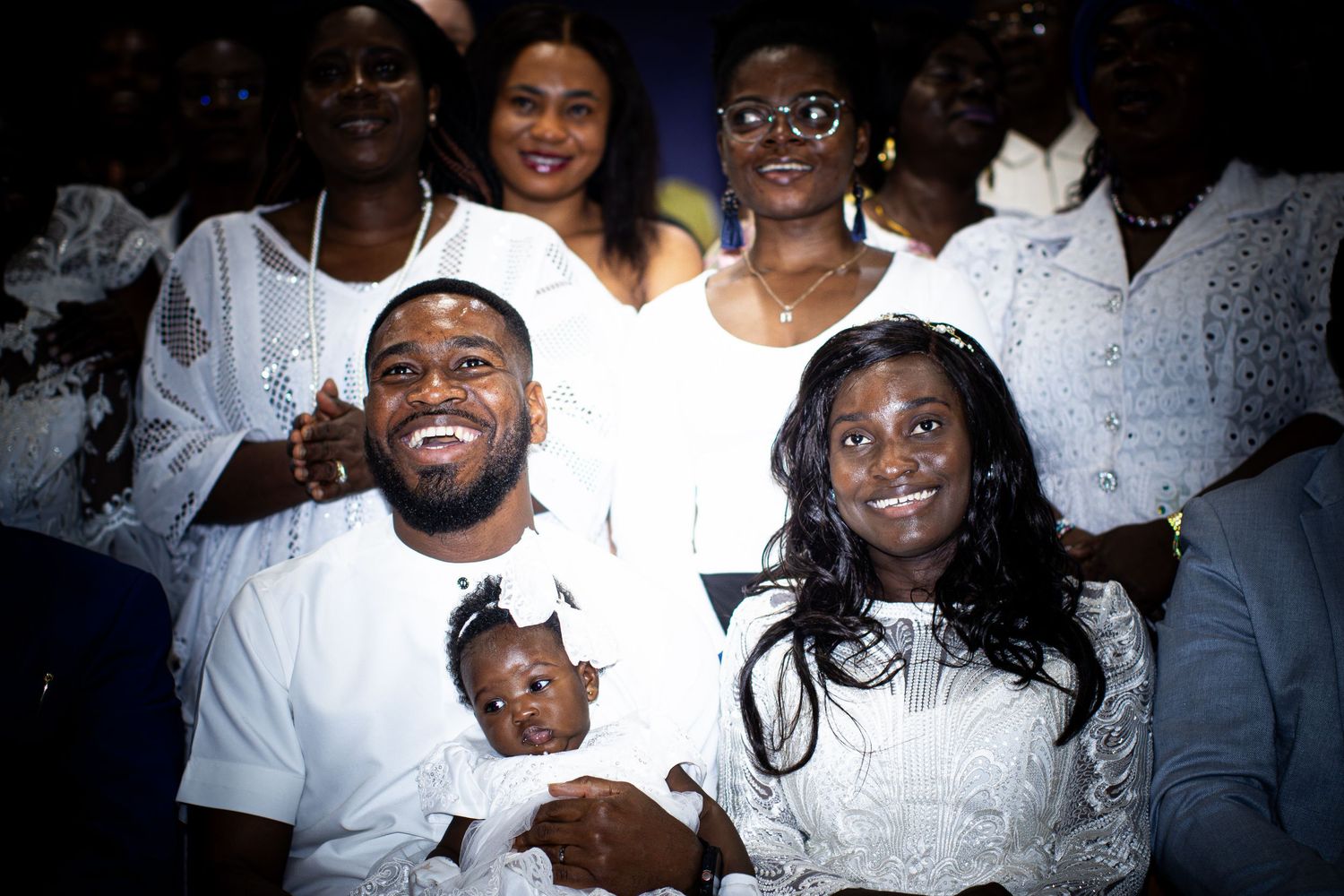 Family dressed in white poses together smiling at a group celebration event.