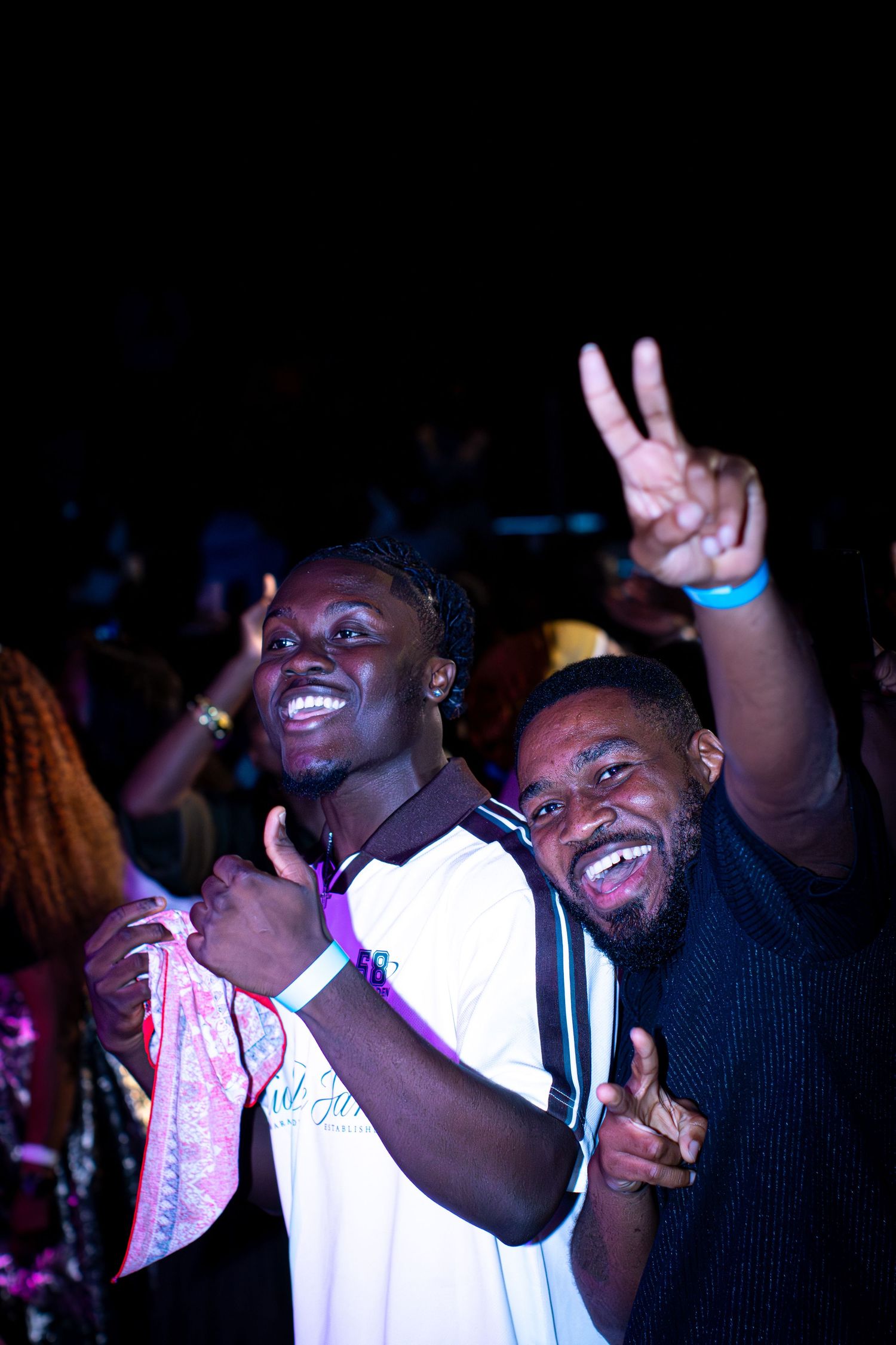 Two young men smile and pose with peace sign at nighttime event.