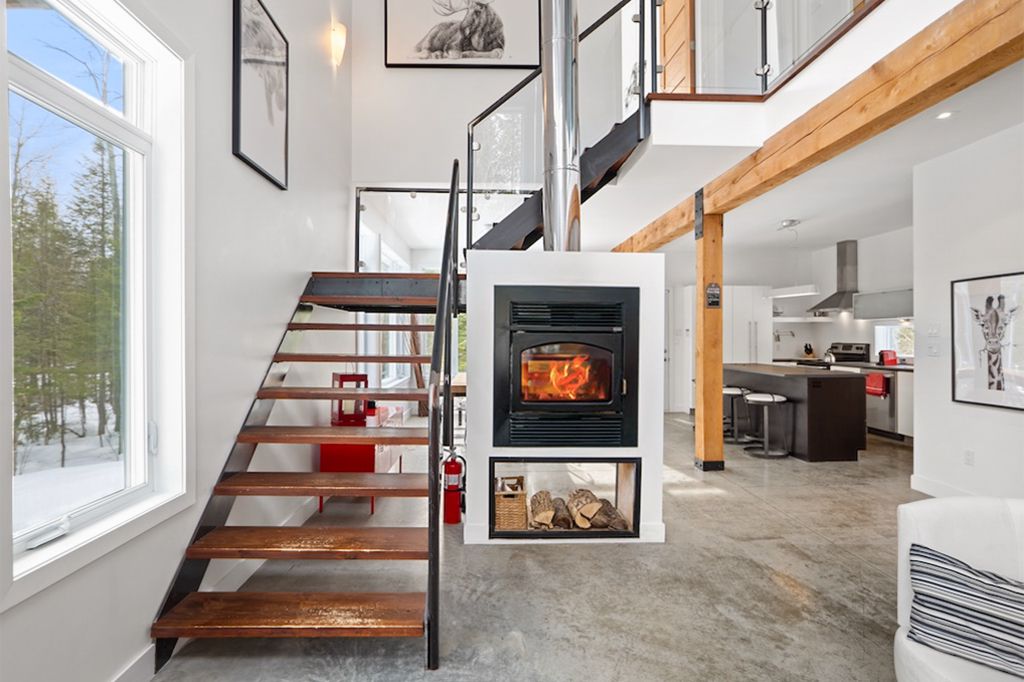 Modern chalet interior with open staircase, wood-burning fireplace, and exposed timber beams.