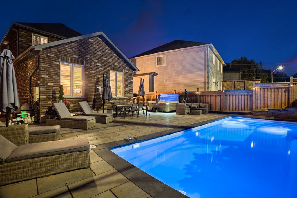 Stunning backyard pool illuminated at night with patio seating and outdoor kitchen area.