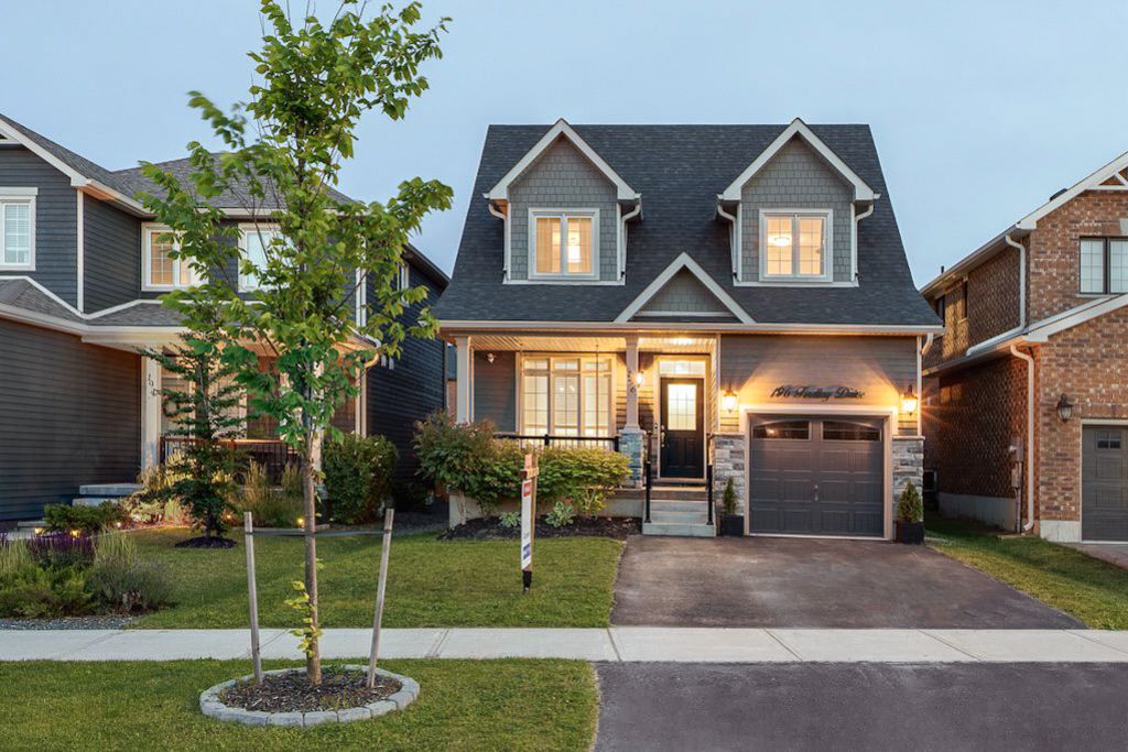 Charming grey craftsman-style home with stone accents, manicured landscaping, and a  garage at dusk.