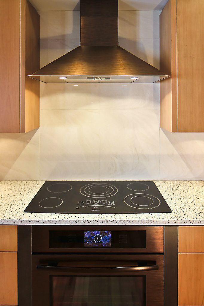 Modern kitchen featuring black electric cooktop, stainless steel range hood, wood cabinets, and granite countertop.