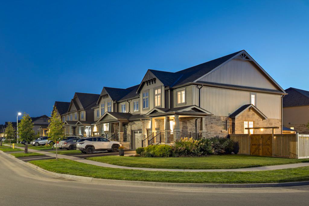 Row of elegant two-story suburban townhomes with stone and stucco exteriors photographed at twilight.