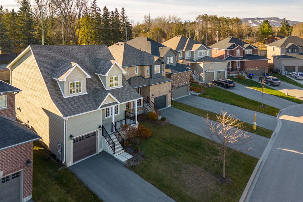Aerial view of suburban neighborhood with beige two-car garage home, manicured lawns, and mature trees in autumn.