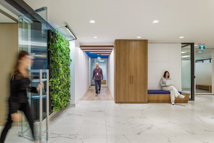 Modern office hallway with a vertical green living wall, marble floors, and employees walking past wood pod.