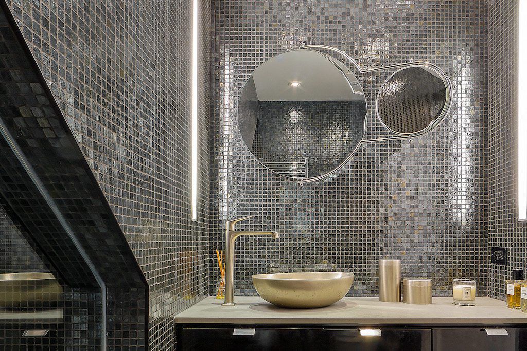 Glamorous bathroom with silver mosaic tile walls, round mirrors, and a gold vessel sink.