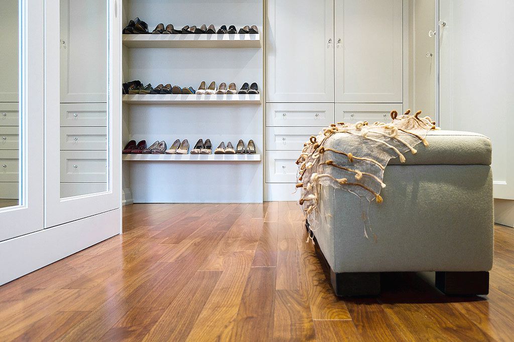 Spacious walk-in closet with built-in shoe shelves, white cabinetry, and warm hardwood flooring.