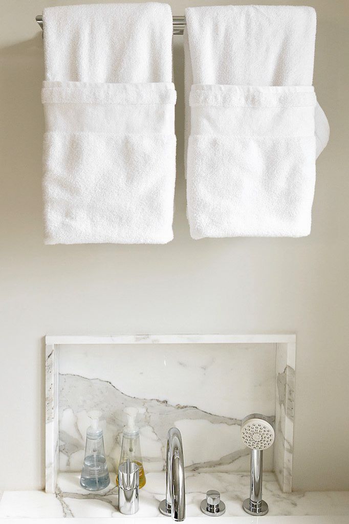 Elegant marble bathtub surround with chrome fixtures and white folded towels on a towel bar above.