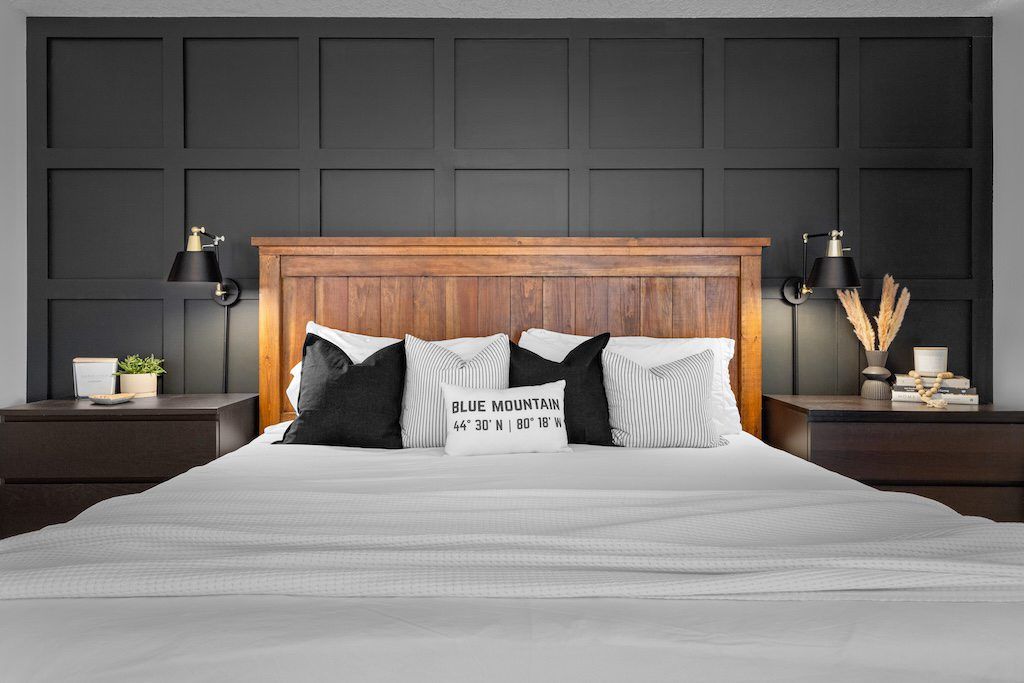 Elegant bedroom with wooden headboard, black and white pillows, and dark geometric accent wall.