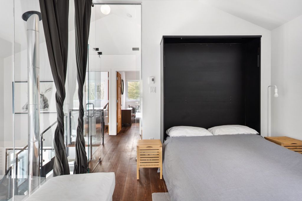 Minimalist bedroom with Murphy bed, black accent wall, white walls, and light wood furnishings.