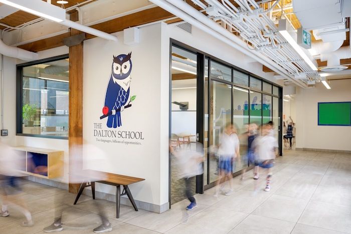 The Dalton School entrance with owl logo, glass walls, and blurred students walking through a modern corridor.