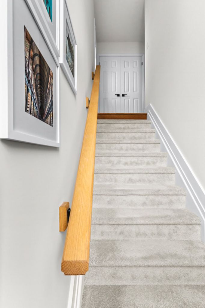 Carpeted staircase with oak wood handrail, white walls, and framed artwork leading to upper floor.