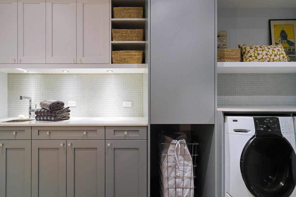 Modern laundry room with gray cabinetry, white subway tile backsplash, and front-loading washing machine.
