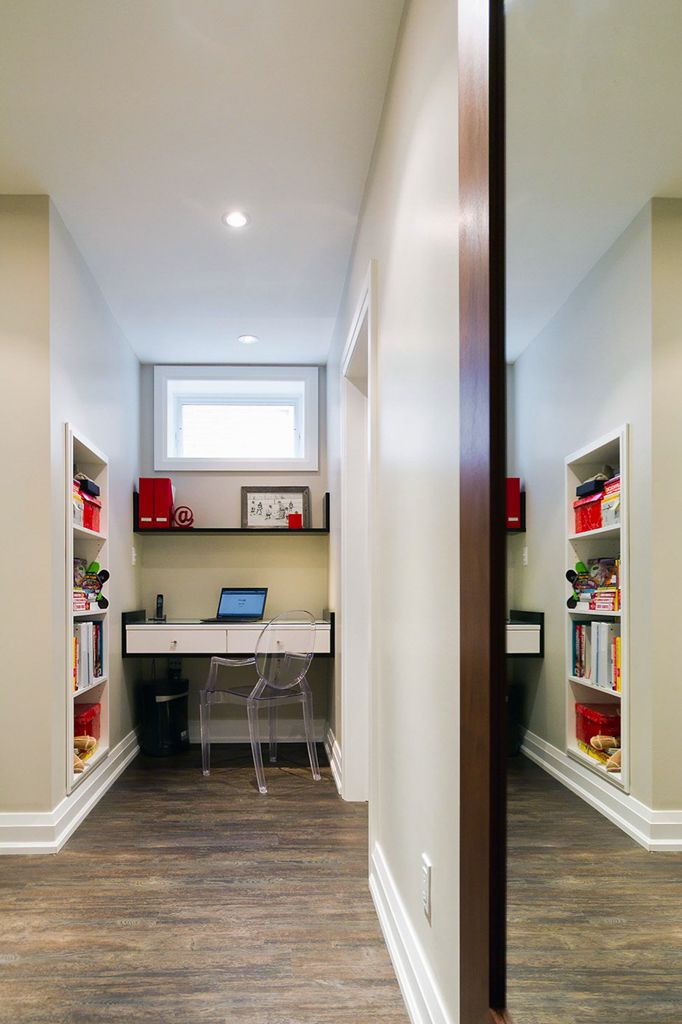 Narrow home office nook with built-in bookshelves, floating desk, laptop, and small window in basement hallway.