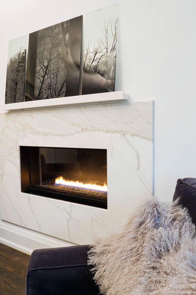 Modern marble fireplace with linear gas flames, white mantel shelf, and black-and-white tree artwork above.