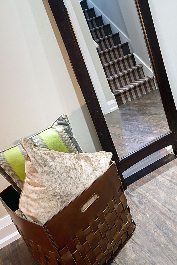 Entryway with woven leather basket holding decorative pillows beside a large mirror reflecting carpeted staircase.