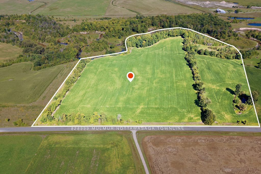 Aerial view of a large green agricultural parcel of land with tree borders and road access.