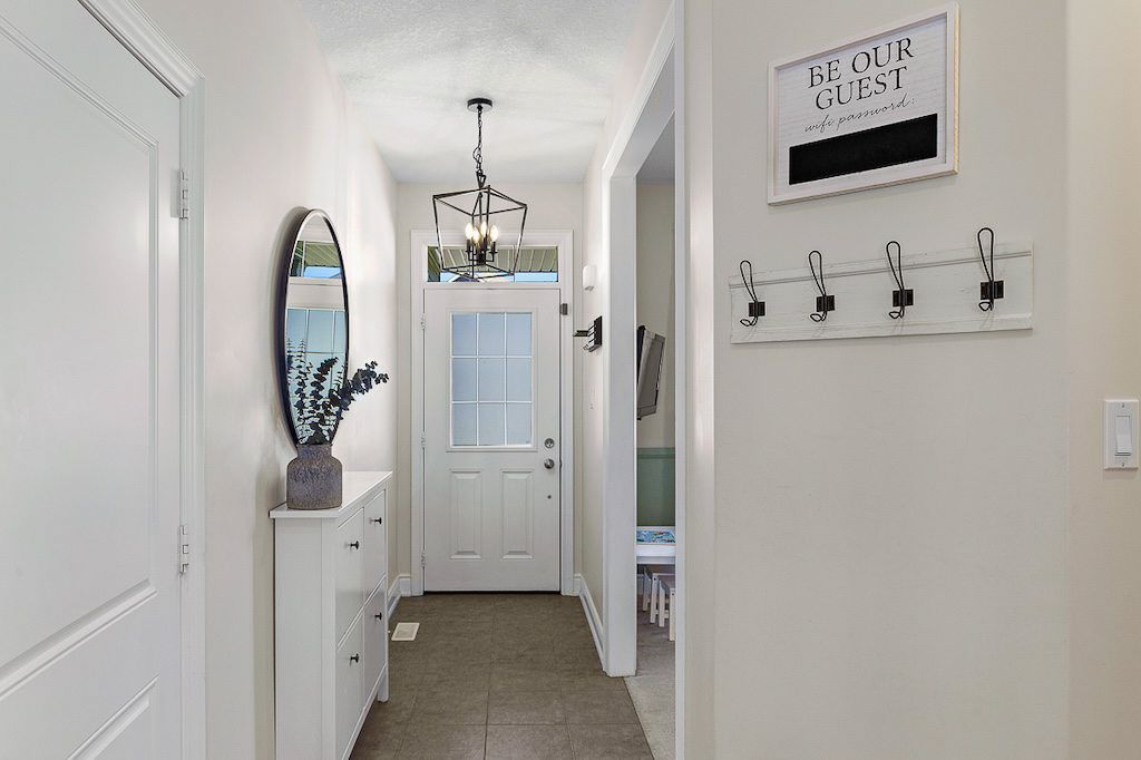 Bright white entryway hallway with chandelier, oval mirror, coat hooks, and Be Our Guest decorative sign.