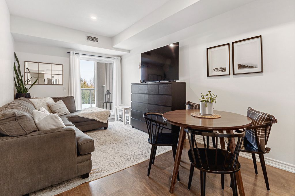 Bright open-plan living and dining area with sectional sofa, round table, dark dresser, and balcony access.