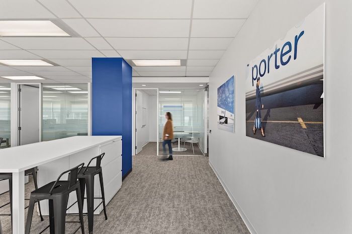 Porter Airlines office corridor with blue accent wall, branded artwork, standing desk, and open workspace.