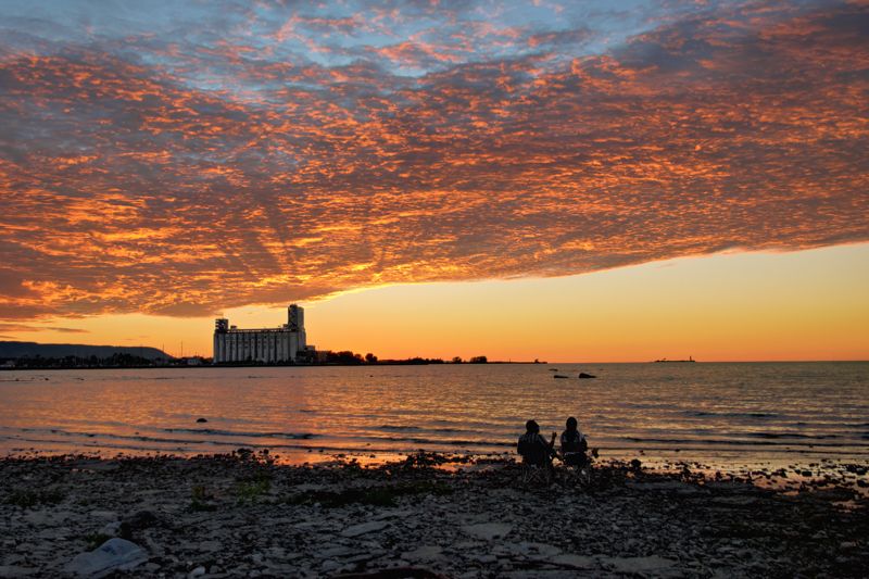 Two people sitting at Sunset Point watching a brilliant orange sunset behind the terminals in Collingwood Ontario