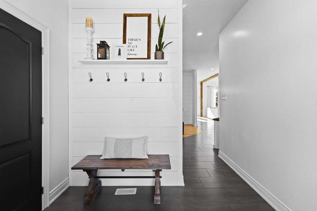 Farmhouse mudroom with white shiplap wall, wooden bench, coat hooks, and dark tile flooring.