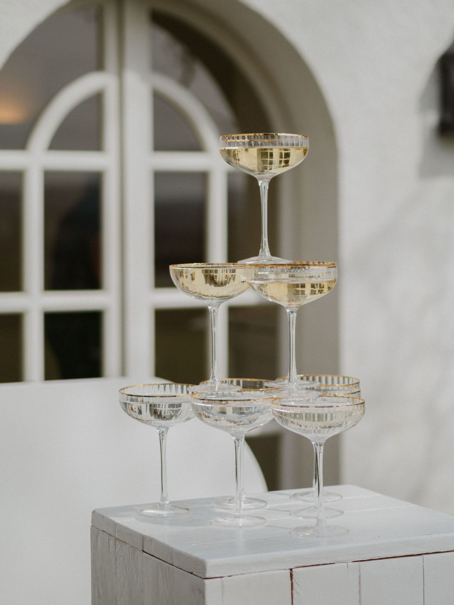 White tiered display with vintage champagne coupes arranged in a modern minimalist setting.