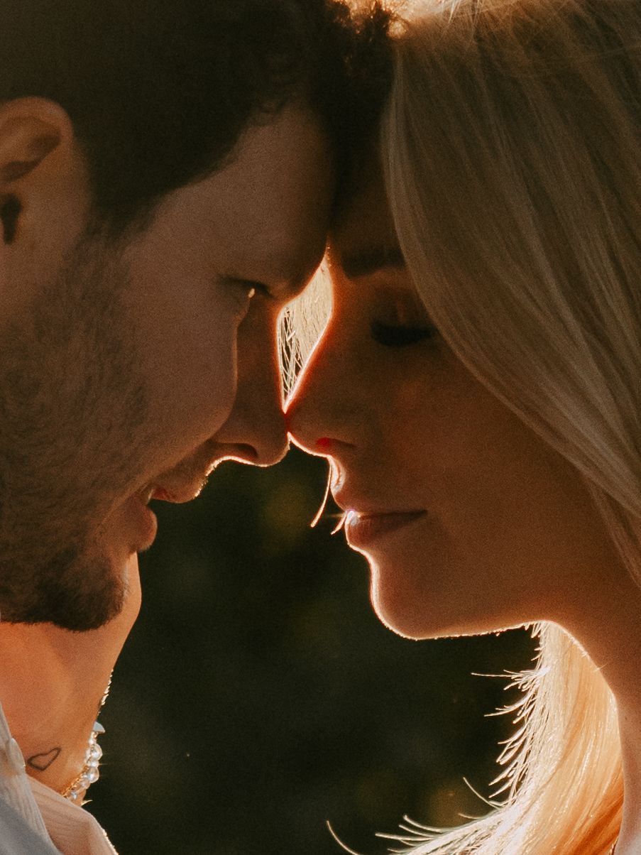 Intimate close-up silhouette of a couple in golden sunlight with their faces nearly touching in a romantic moment.