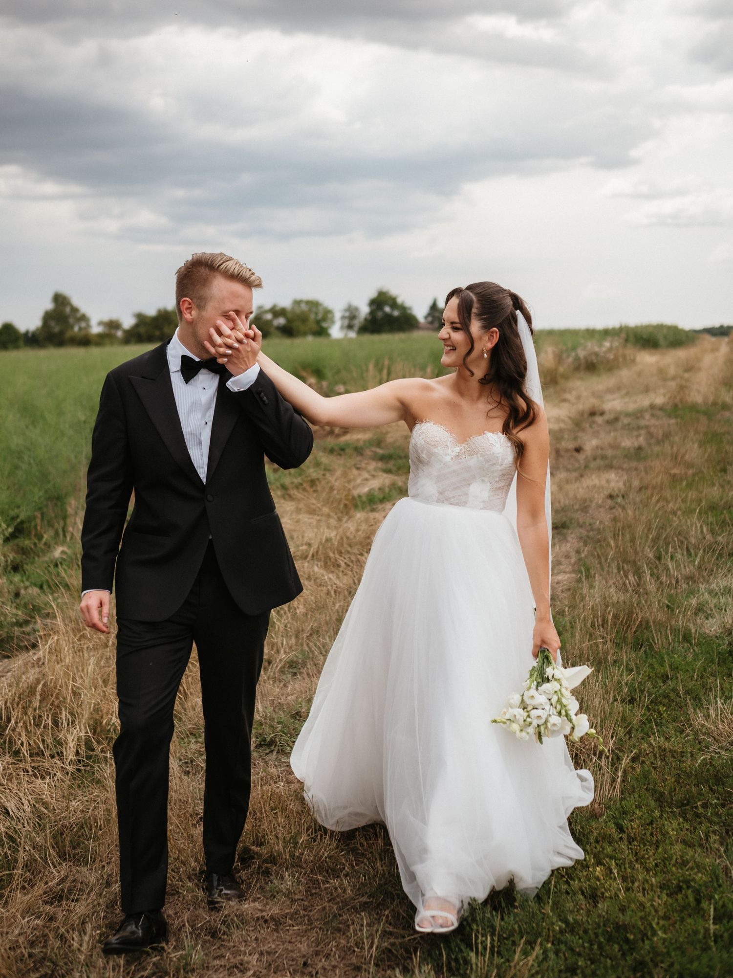 Joyful couple shares candid laughter while walking together in a rustic field on their wedding day.