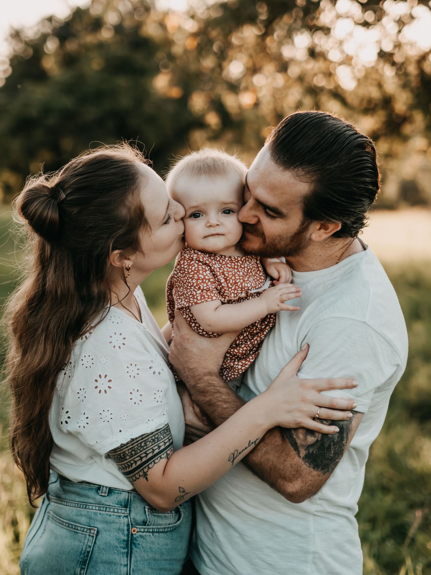 A family shares tender embraces and kisses in a sunlit outdoor setting during a candid photo session.