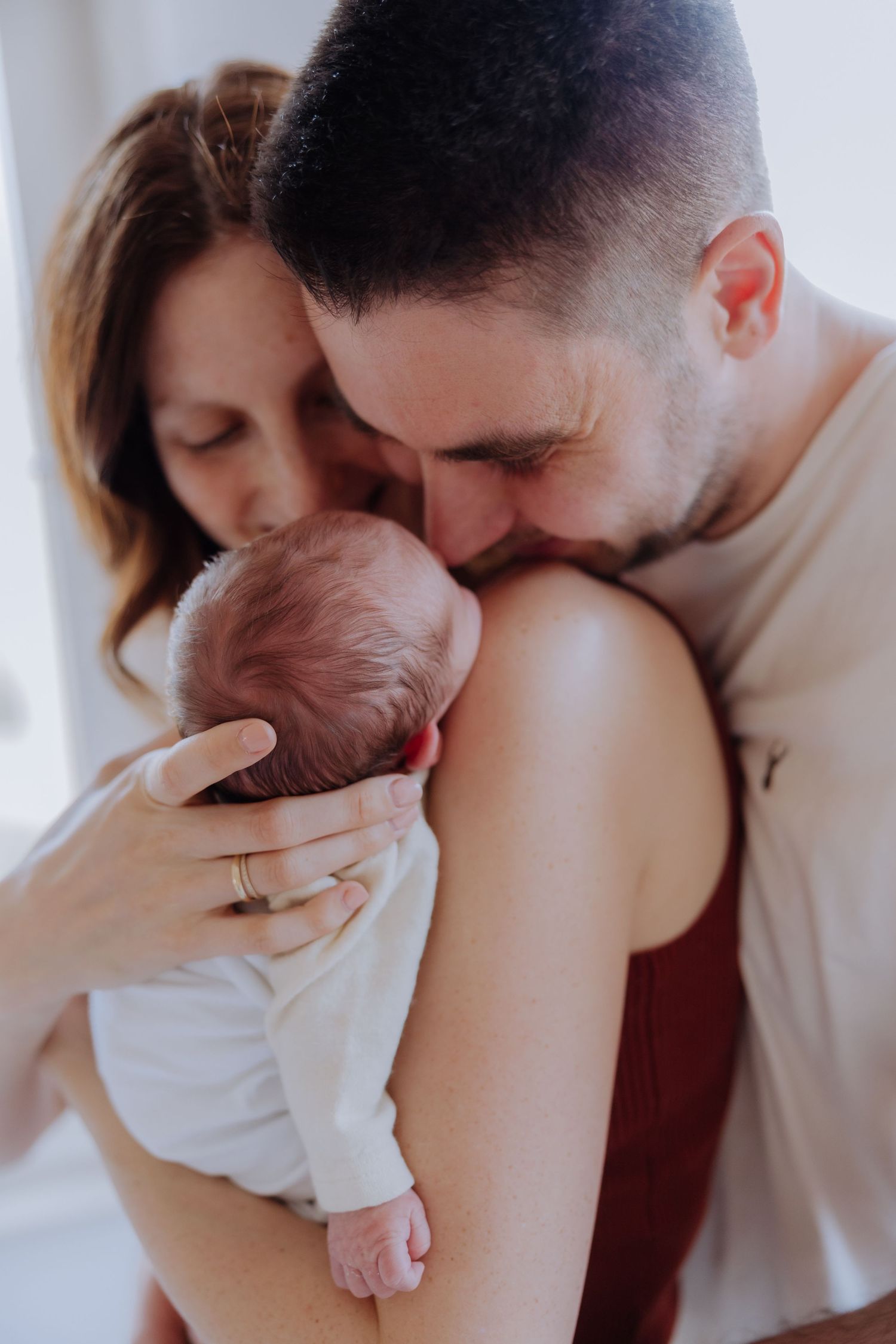 New parents tenderly kissing their sleeping newborn baby, sharing a precious family moment together.