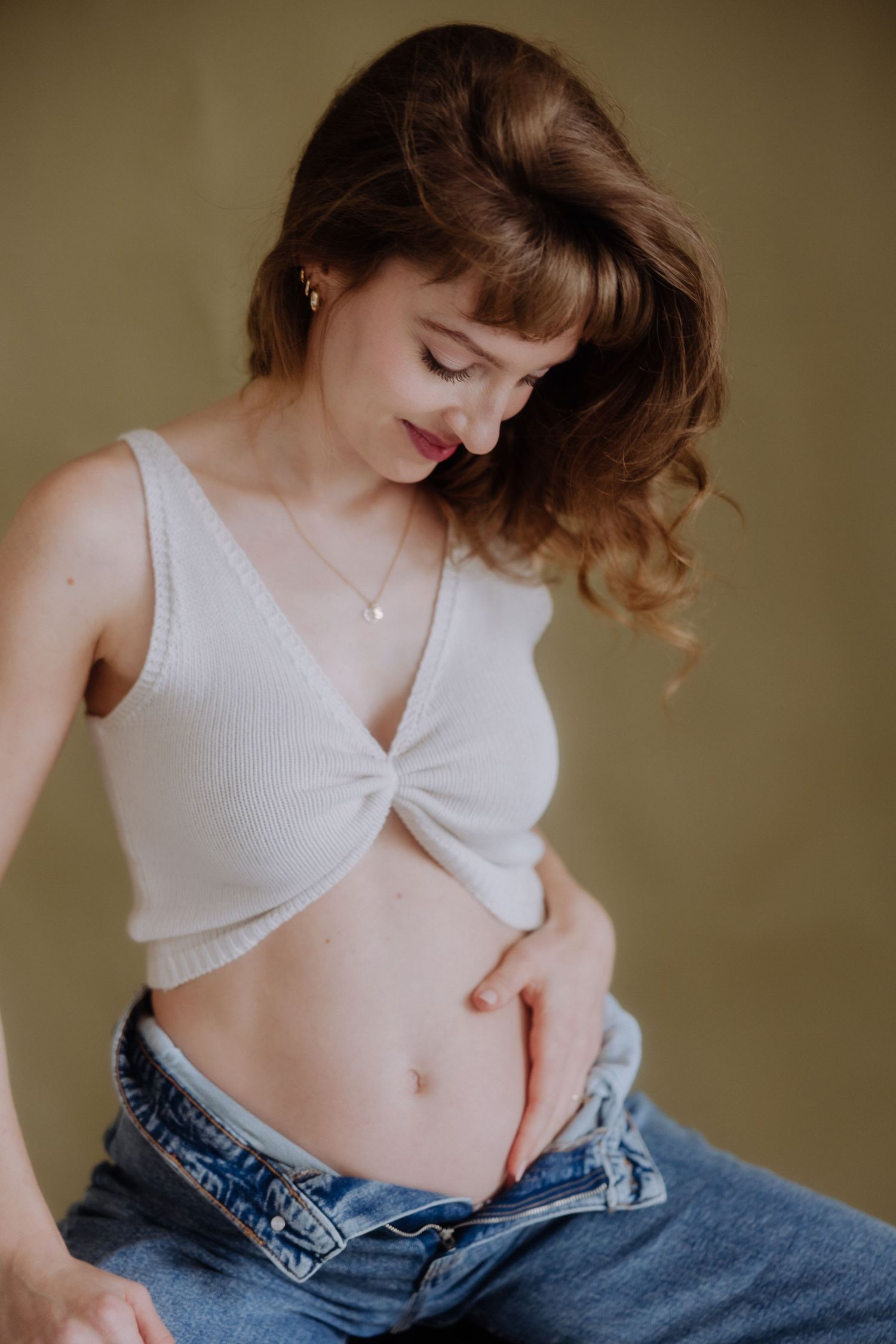 Artistic fashion portrait showing white cropped top and denim jeans in soft warm lighting.