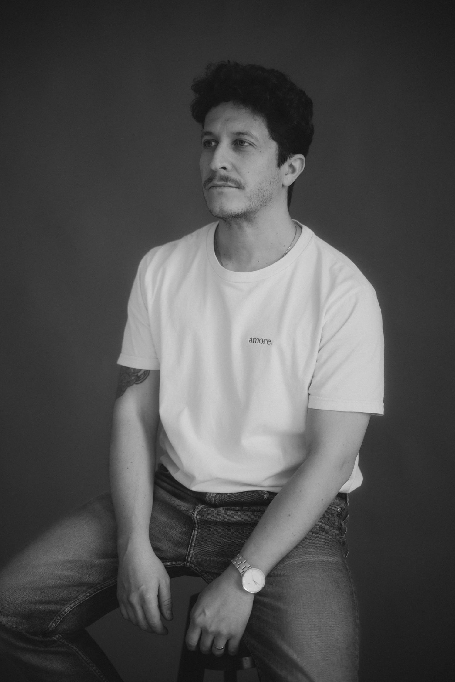 A black and white photo series showing someone in a white t-shirt and dark pants sitting against a dark background.