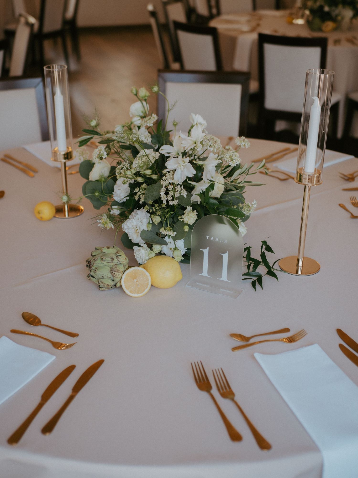 Elegant table settings with gold flatware, white linens, and citrus fruit centerpieces create a sophisticated dining atmosphere.