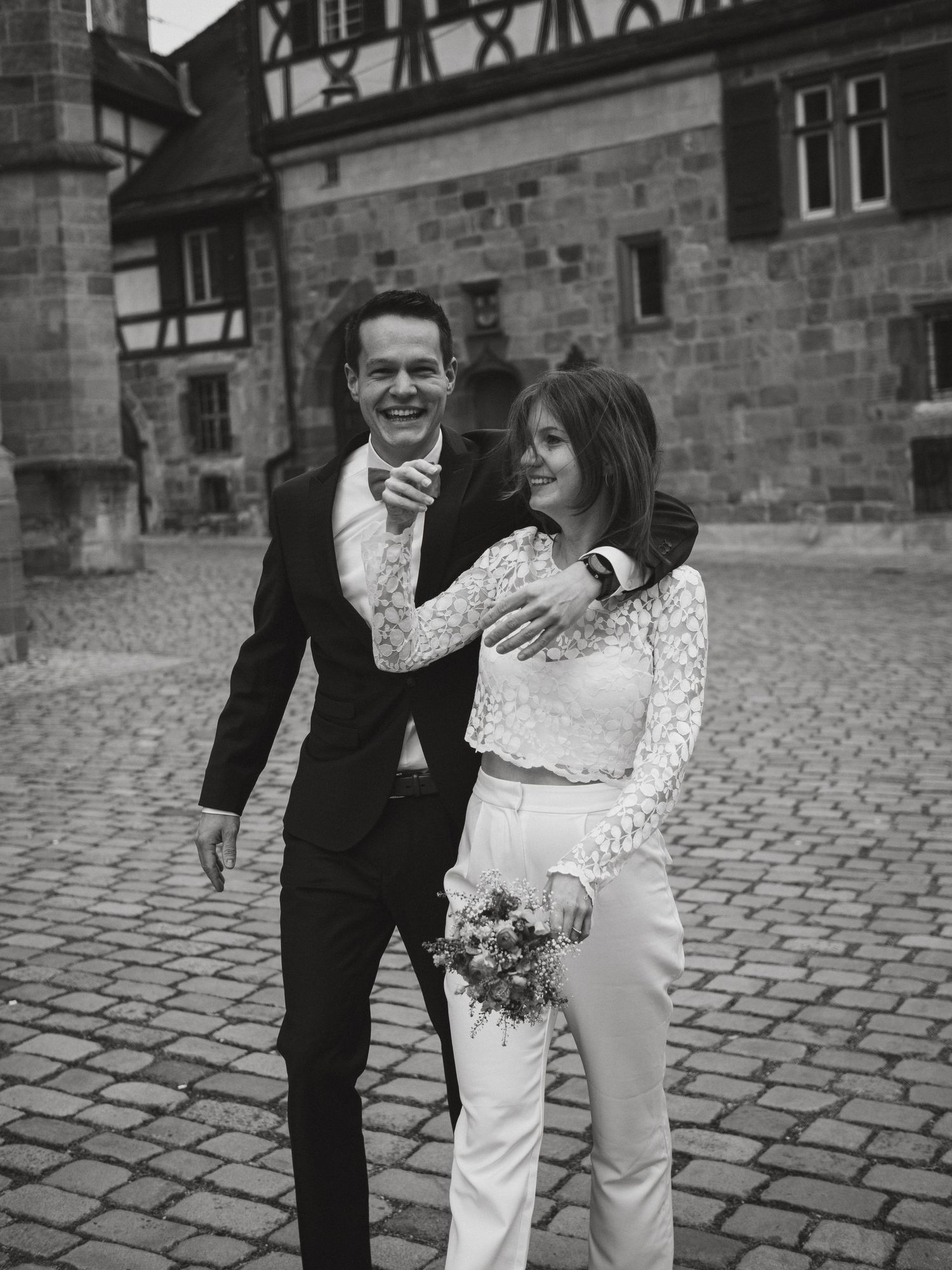 A couple shares a joyful moment on cobblestone streets in front of historic timber-framed buildings.