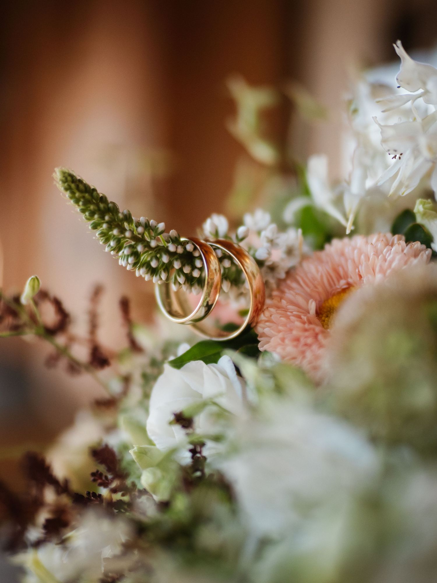 Wedding rings nestled among soft pink and white flowers with delicate green foliage in a romantic macro shot.