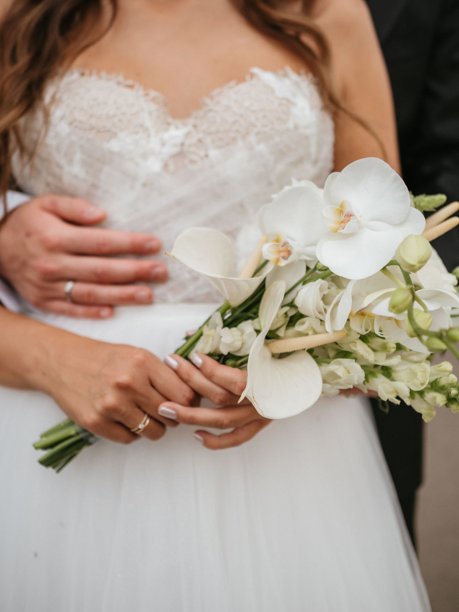 Elegant white orchid and greenery wedding bouquet held against a white bridal gown.