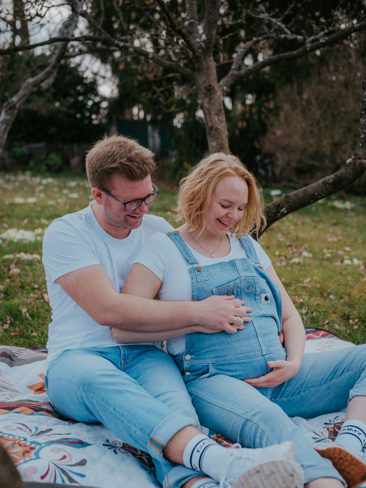 A couple in denim overalls relaxes together on a blanket outdoors during a casual photoshoot.