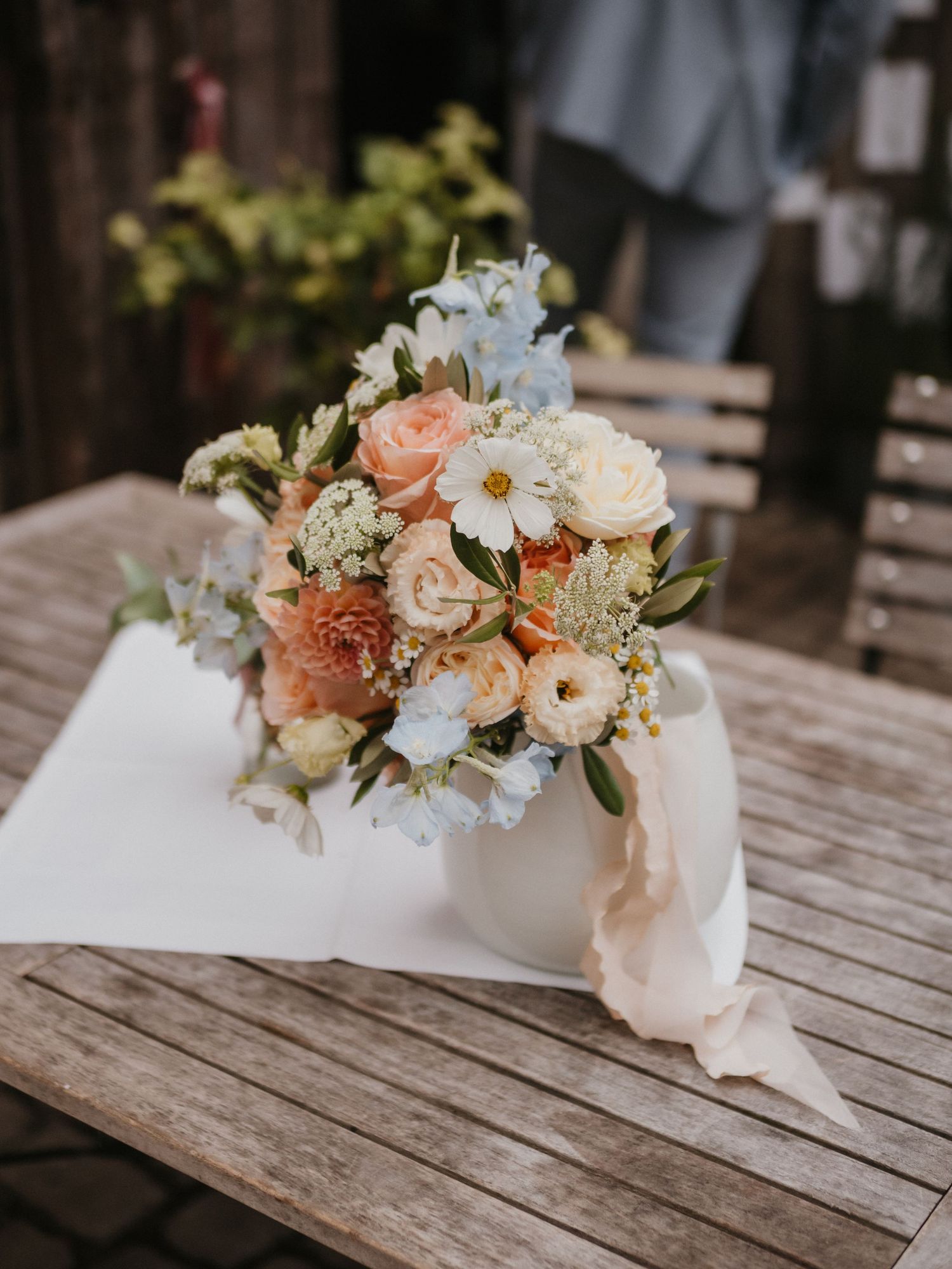 Delicate floral arrangement with peach roses and white daisies on rustic wooden table creates romantic wedding decor.
