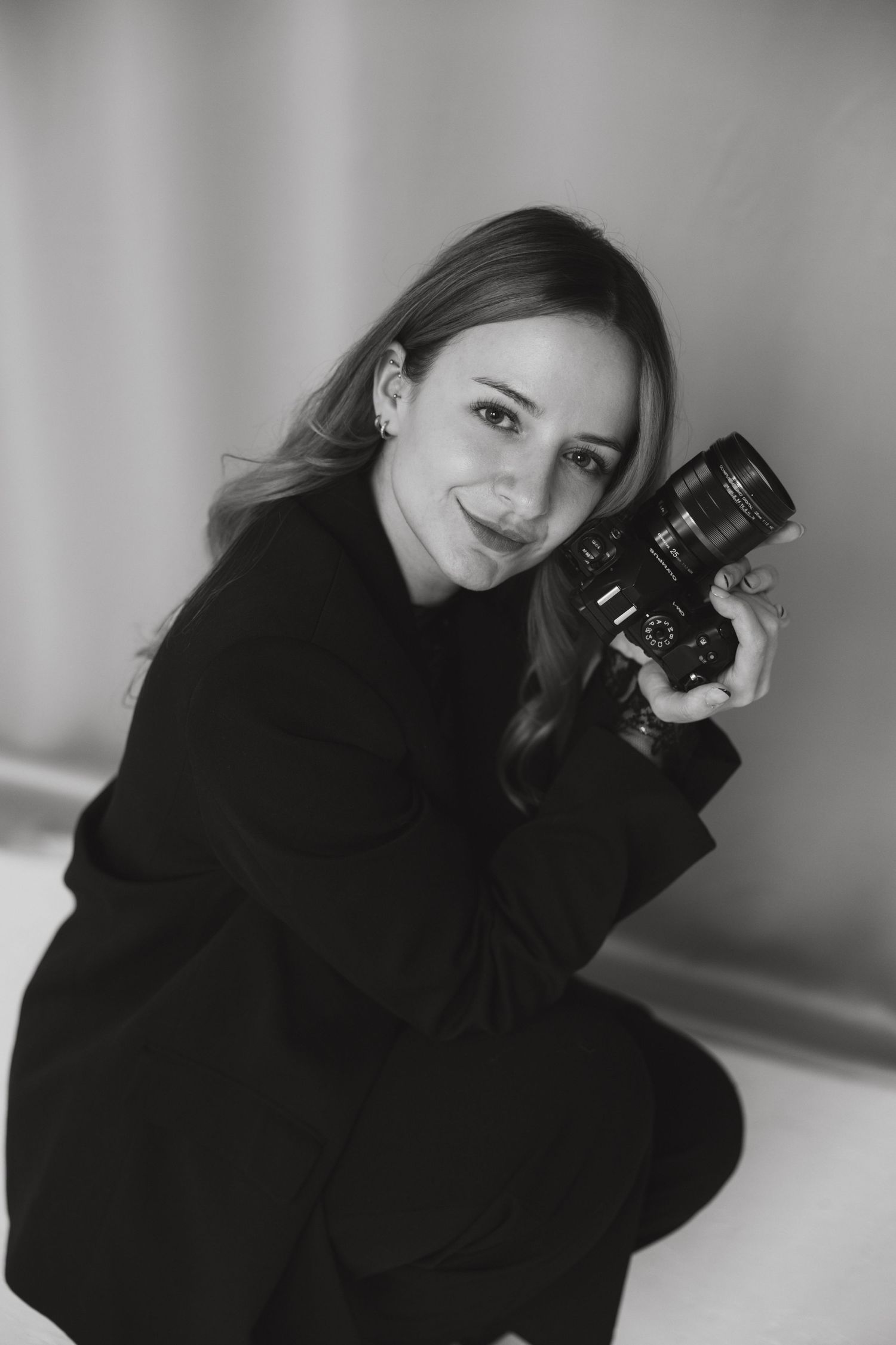 Black and white photo series of photographer in dark sweater posing with vintage camera against light background.