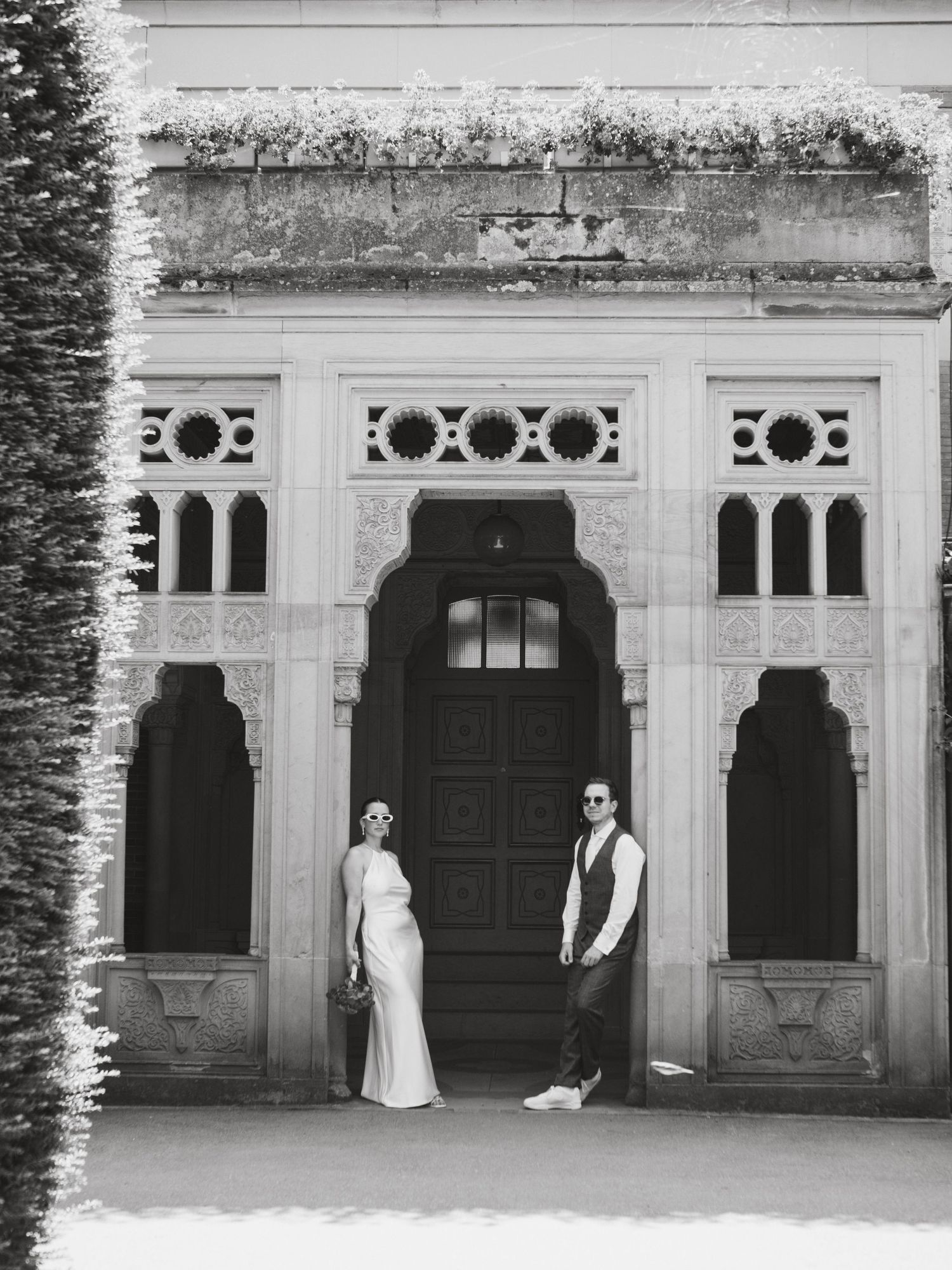 Elegant black and white architectural photograph showing a couple posing in front of an ornate vintage doorway.