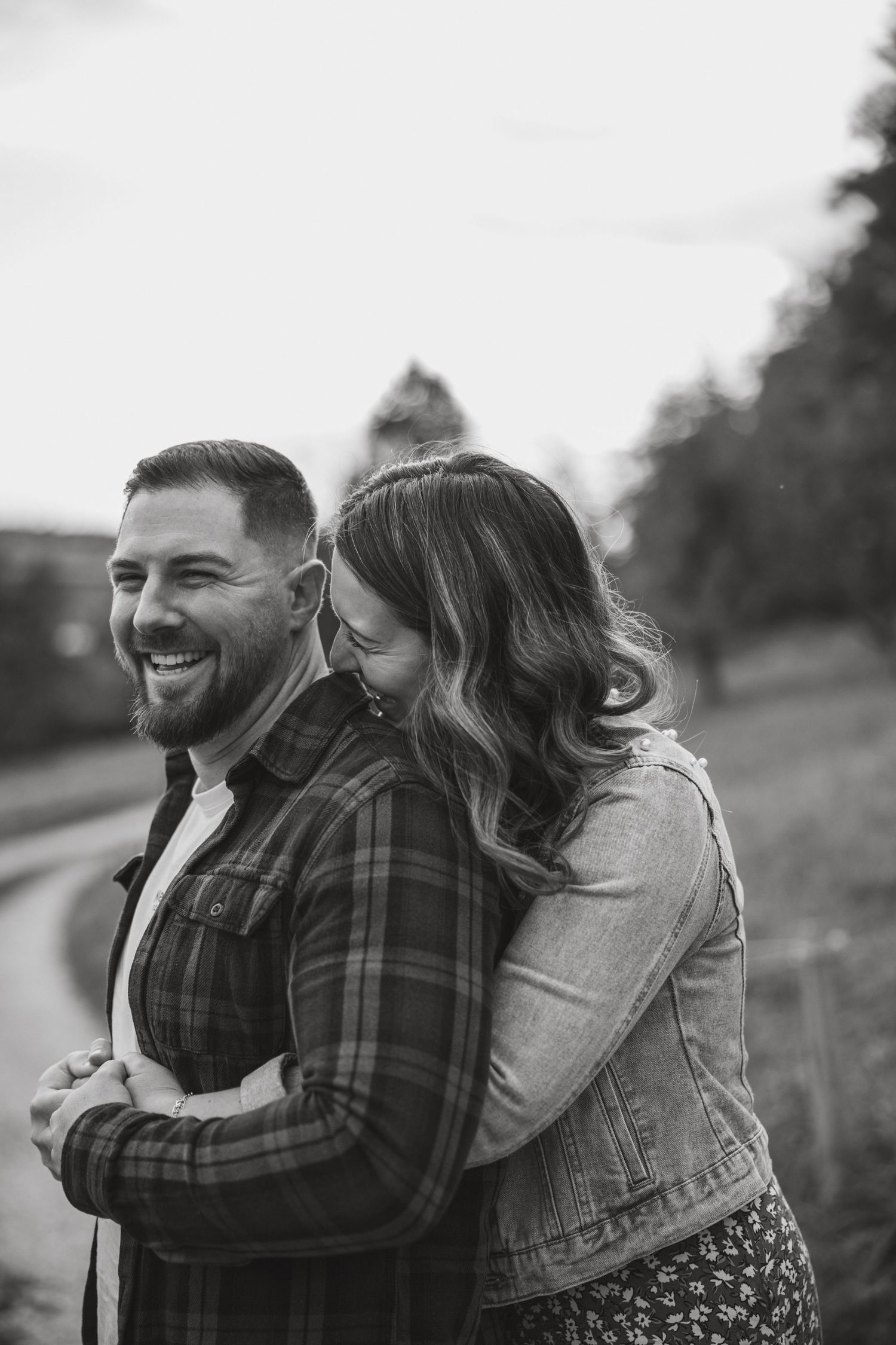 A couple embraces and laughs together in a field during a romantic outdoor photo session.