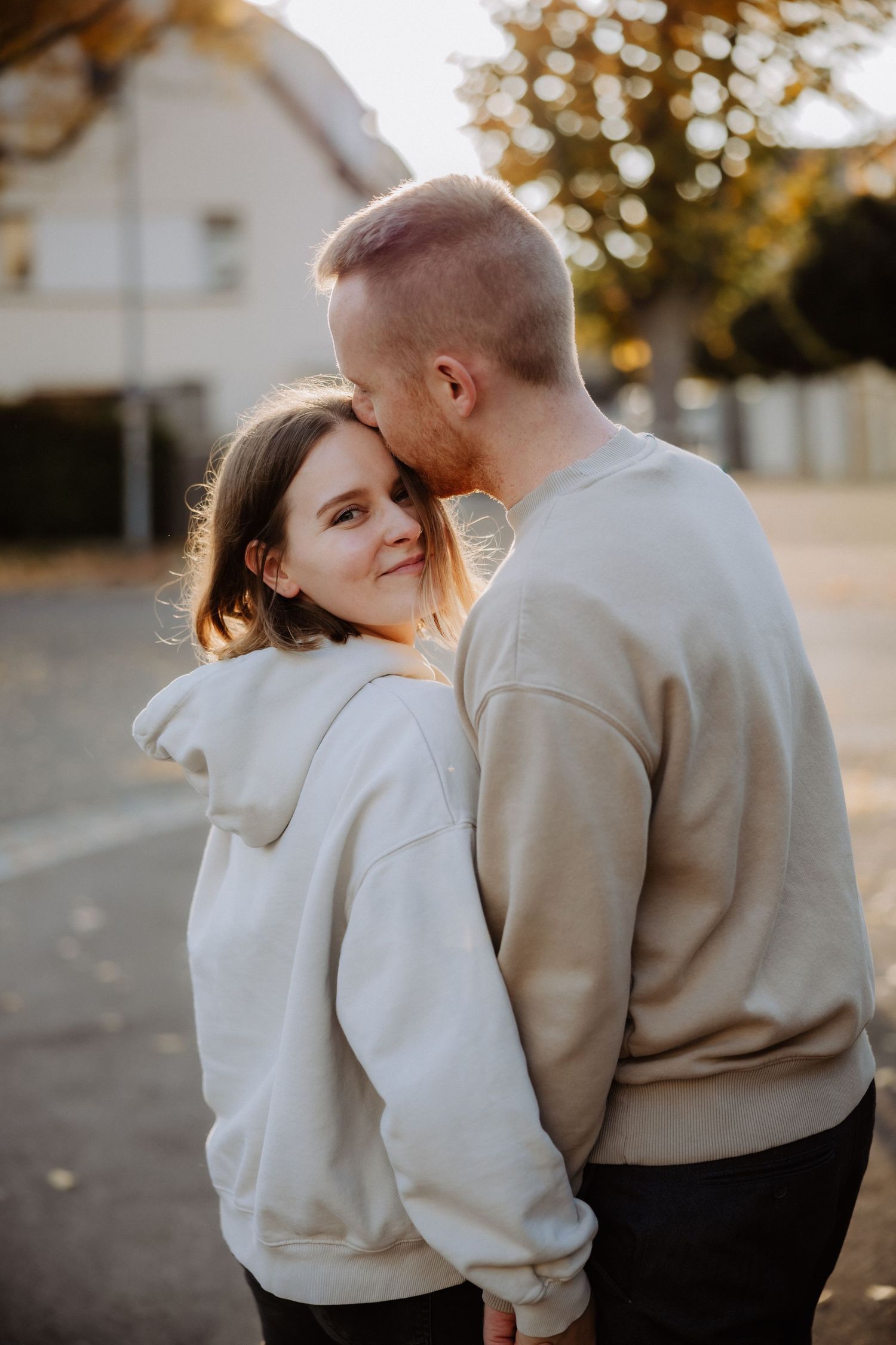 A romantic couple in matching beige and white sweaters share tender moments together during a sunset photoshoot.
