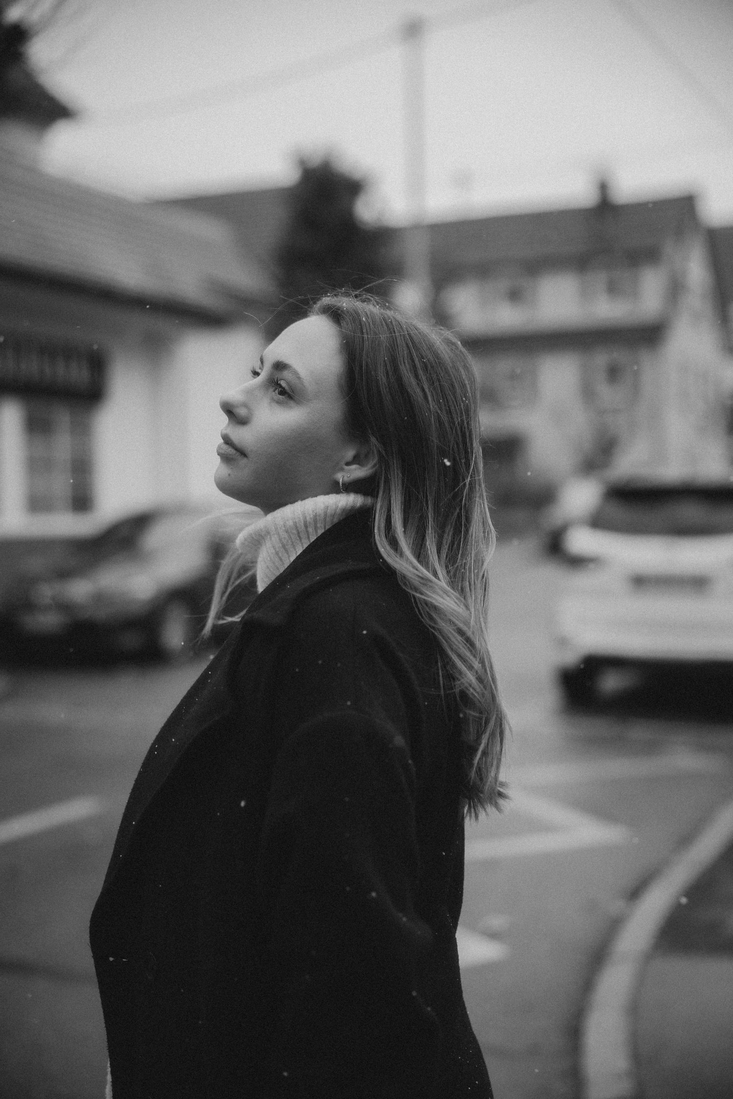 Black and white portrait series showing a person in a dark coat looking upward against a blurred urban background.