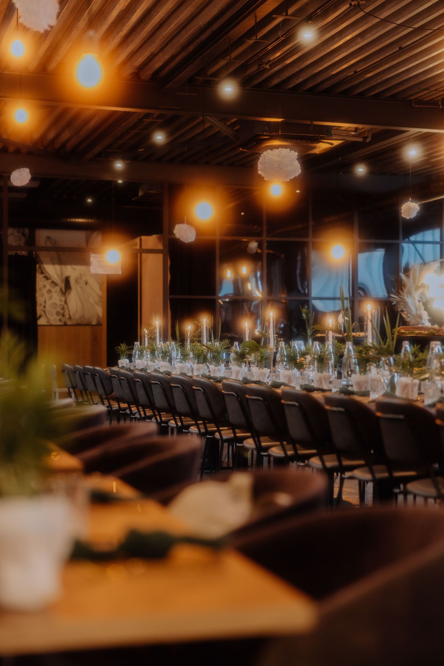 Elegant restaurant interior with warm lighting, wooden ceiling beams, and long dining tables set for a formal event.